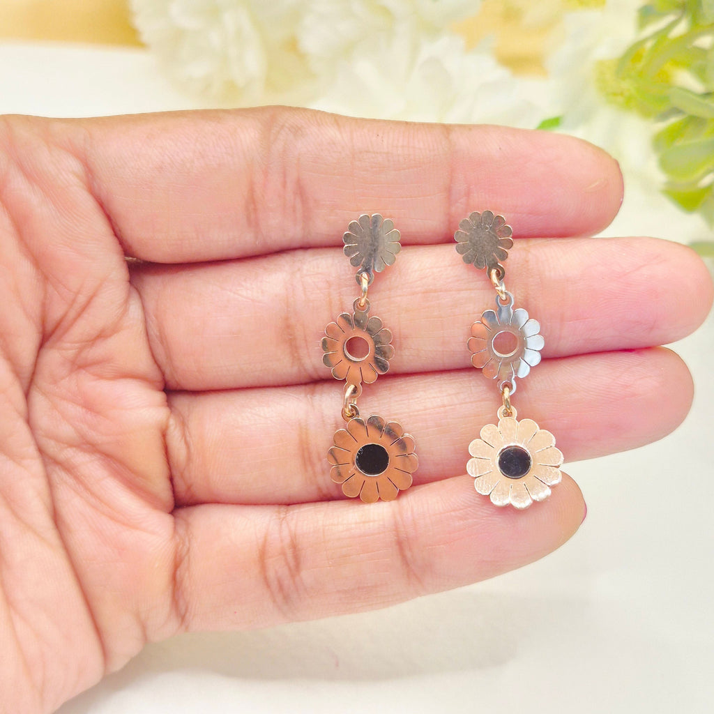 Niomi by Roja gold-tone three-tier floral drop earrings with black enamel centers held in a hand.